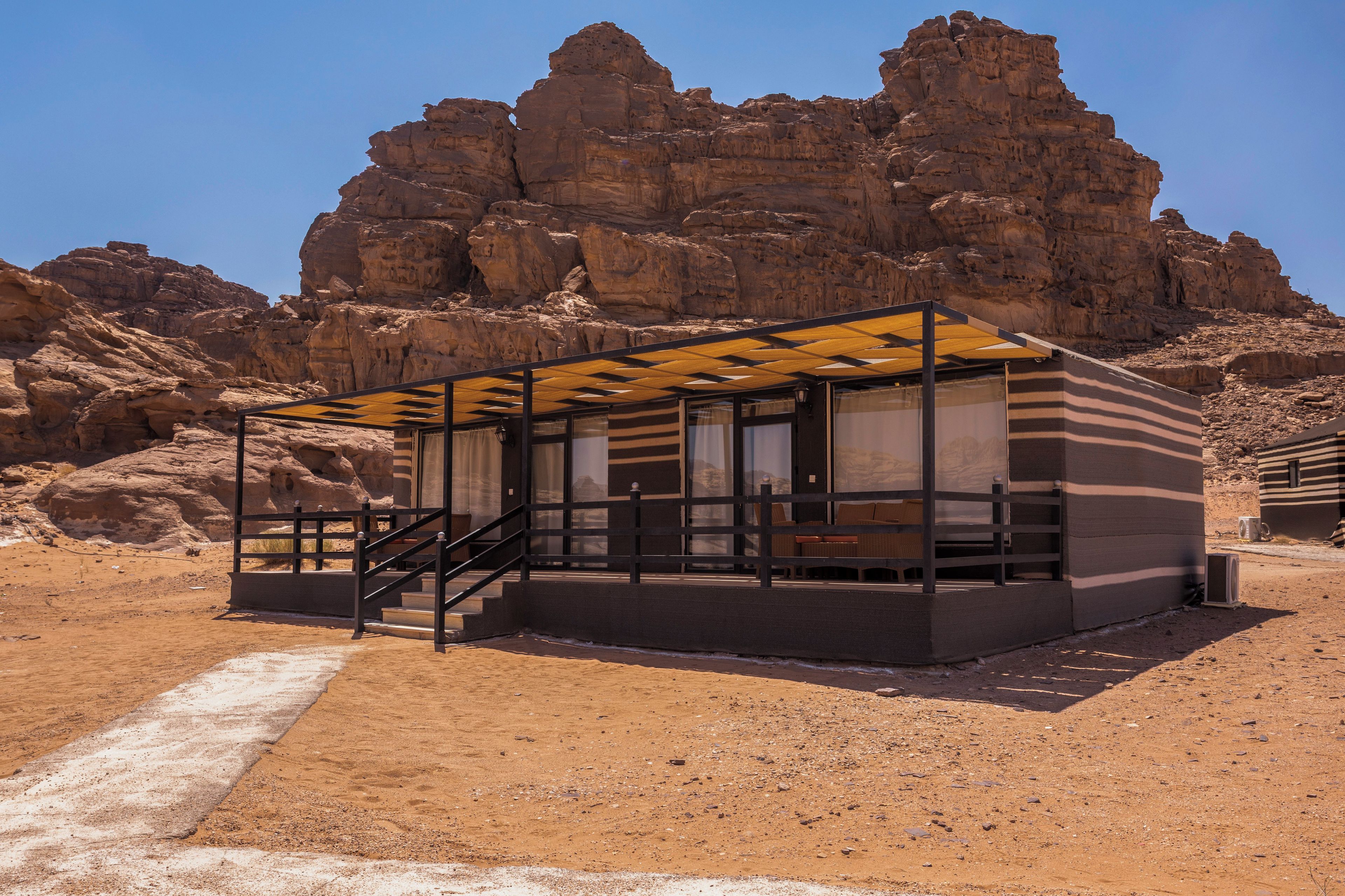 Un bâtiment moderne et minimaliste, doté d’une façade en verre, situé dans un environnement désertique, avec des falaises rocheuses en arrière-plan.