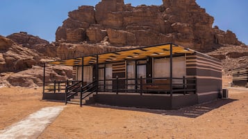A modern, minimalist building with a glass facade, situated in a desert environment with rocky cliffs in the background.