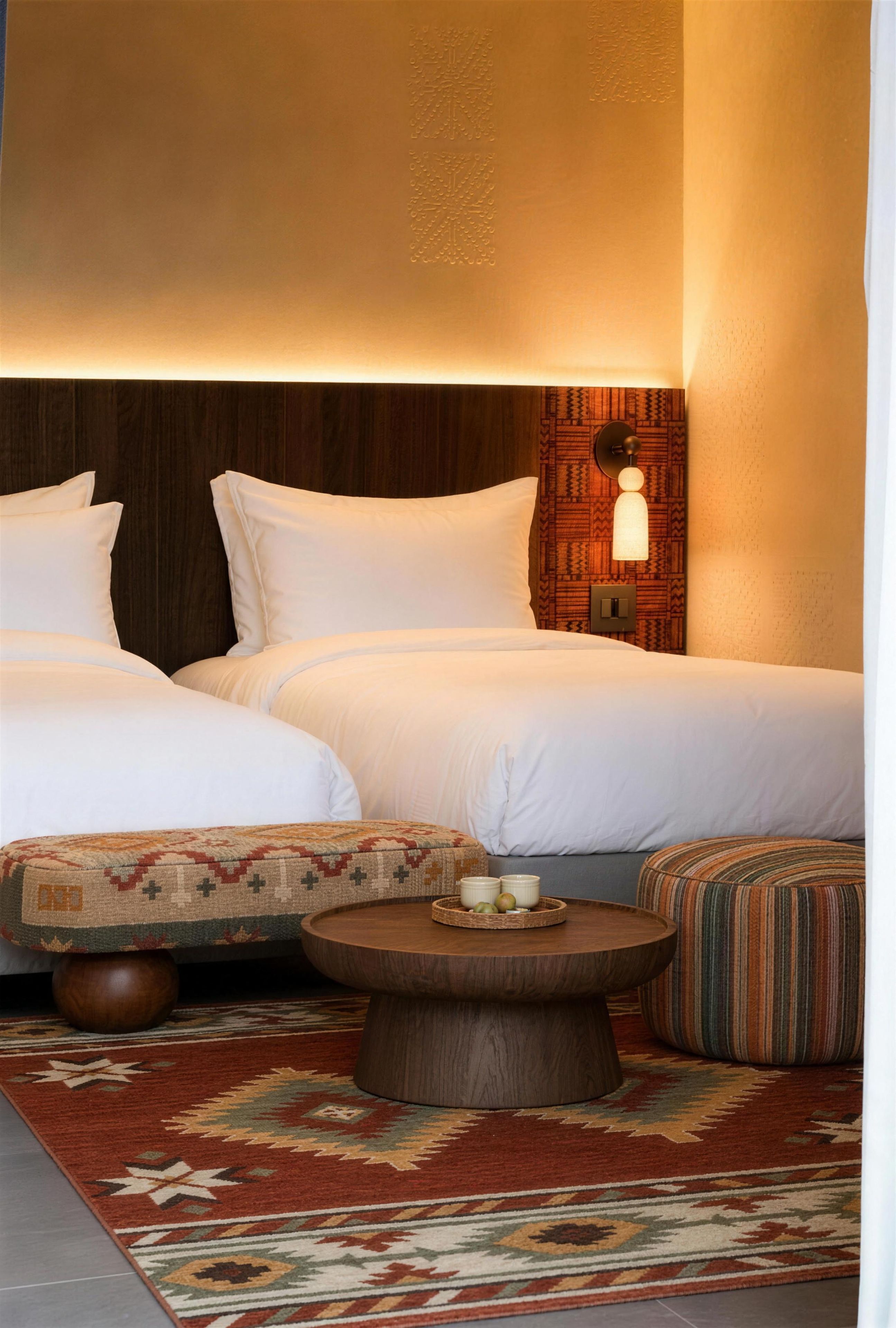 A hotel room with two beds, a round wooden coffee table, and a patterned rug.
