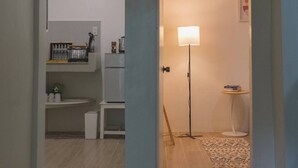 A hallway with a kitchen area on the left, a standing lamp, and a small table with books. - Caalan Cottage (El Nido)