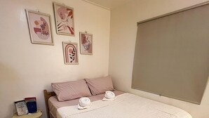 A bedroom with a large bed, a bedside table, a rug, and wall art. - Caalan Cottage (El Nido)