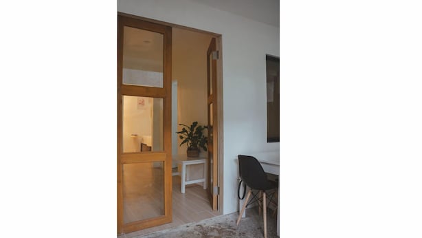 A room with a wooden door leading to another space, a white desk with a chair, and a potted plant. - Caalan Cottage (El Nido)