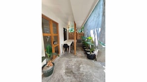 A narrow hallway with a concrete floor, wooden door, and a table with chairs. There are potted plants along the walls. - Caalan Cottage (El Nido)