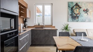 Moderni keittiö, jossa on sisäänrakennettu uuni, pesuallas sekä ruokailutila, jossa on pöytä ja tuolit.