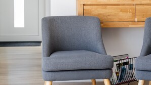Moderni olohuone, jossa seinälle on asennettu litteänäyttöinen televisio. Sen alla on puinen kaappi ja huoneessa on kaksi harmaata nojatuolia, joissa on puujalat.