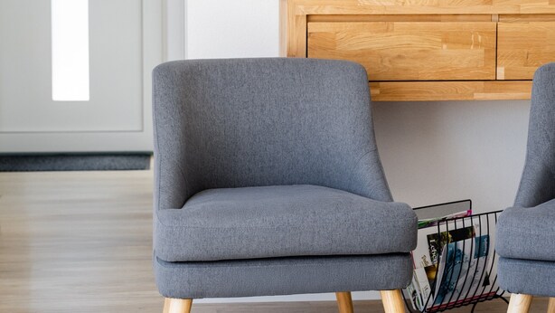 A modern living room with a flat-screen TV mounted on the wall, a wooden cabinet below, and two grey armchairs with wooden legs. - Apartment 'Corner 28' with Mountain View, Private Terrace and Wi-Fi (Oberkirch)