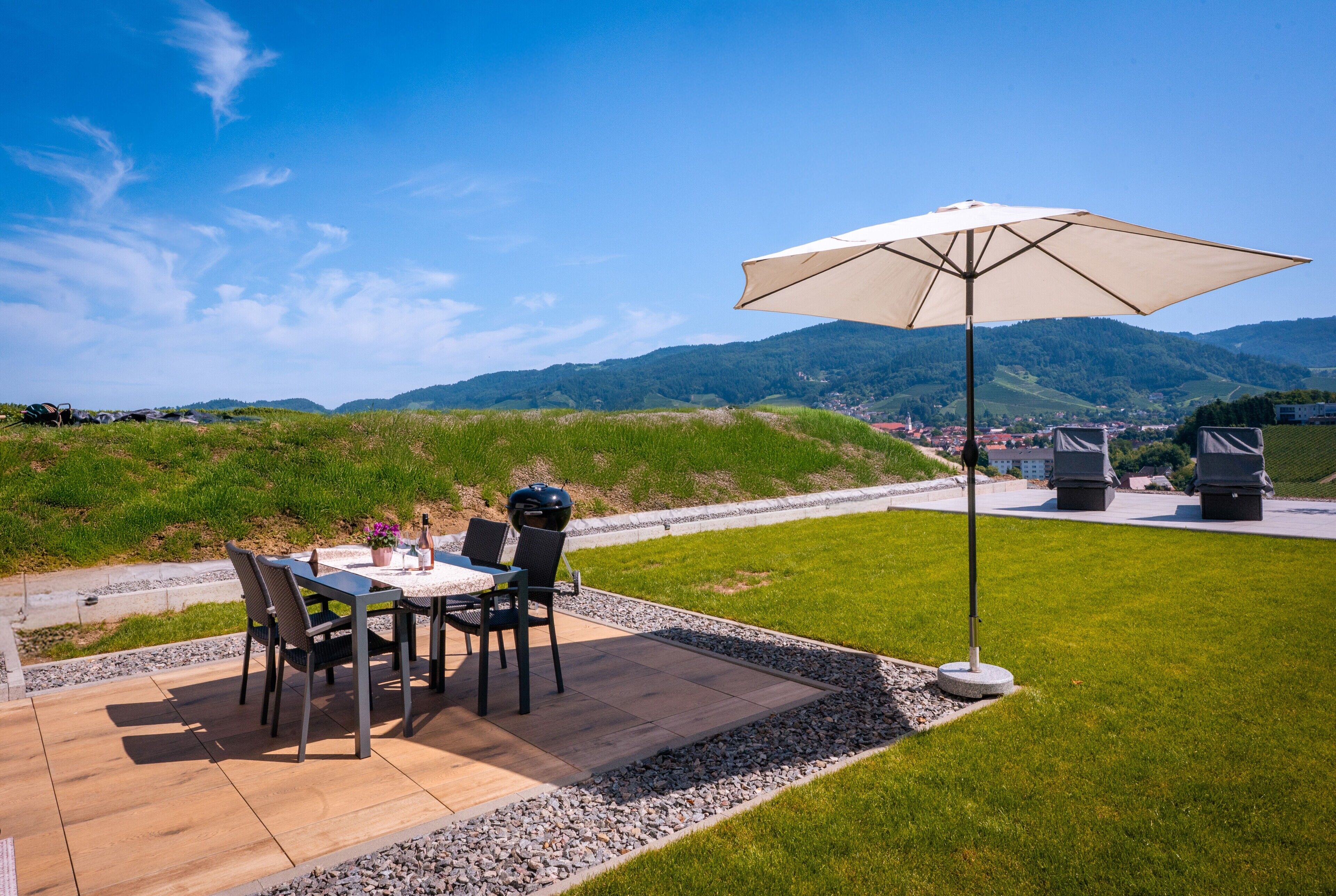 Eine Terrasse im Freien mit Tisch, Stühlen, einem Grill und einem Sonnenschirm.