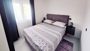 A bedroom with a bed, a nightstand, a lamp, and a window with curtains.