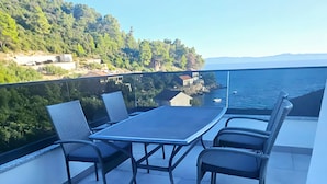 A balcony with a table and chairs, overlooking a coastal area with buildings and greenery.