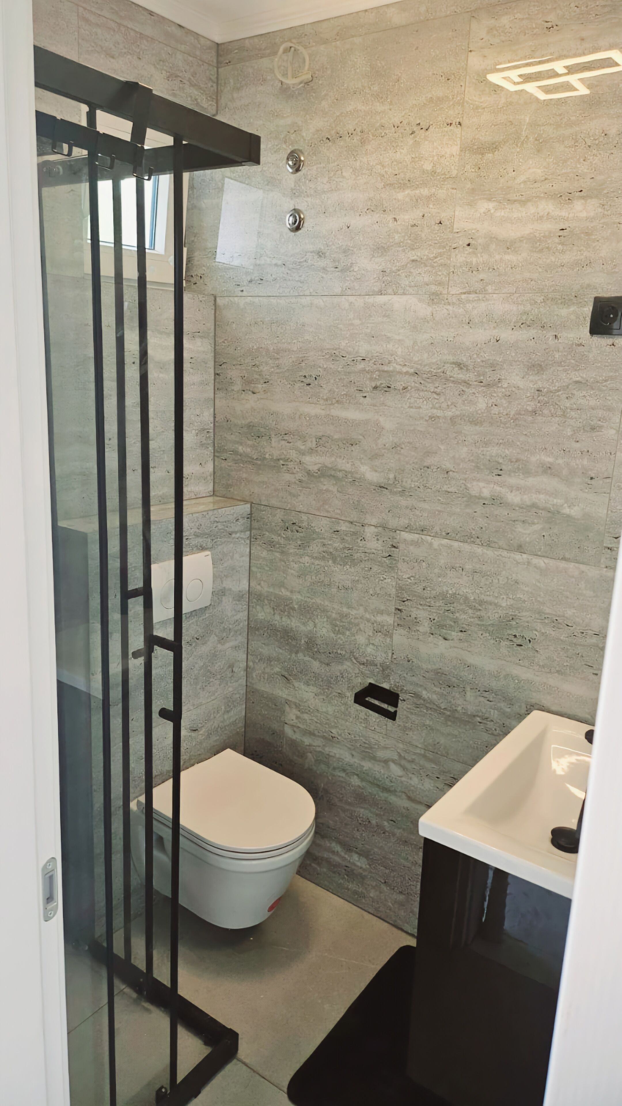 Een moderne badkamer met een glazen douchecabine, toilet en wastafel.