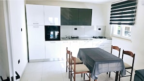 A compact kitchen with white cabinets, a built-in oven, a gas stove, and a window with blinds.