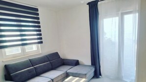 A modern living room with a grey sectional sofa, a glass-top coffee table, and a large window with blinds.