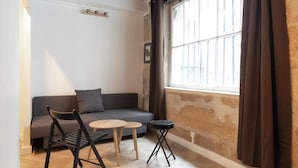 Une pièce chaleureuse avec un canapé gris, deux petites tables rondes et une chaise pliante noire.