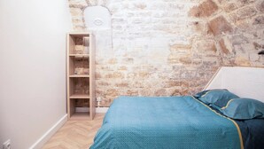 Une chambre avec un mur en pierre, une bibliothèque en bois et un lit avec une literie à motifs.