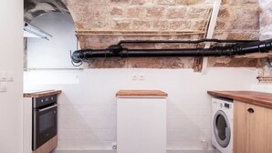 Une cuisine compacte avec un mur en pierre, un lave-linge et un four encastré.