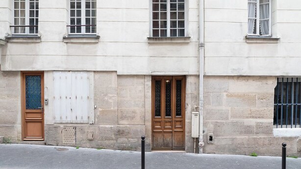 Un bâtiment doté d’une grande porte en bois, d’une porte plus petite avec un portail en métal et d’une fenêtre grillagée.