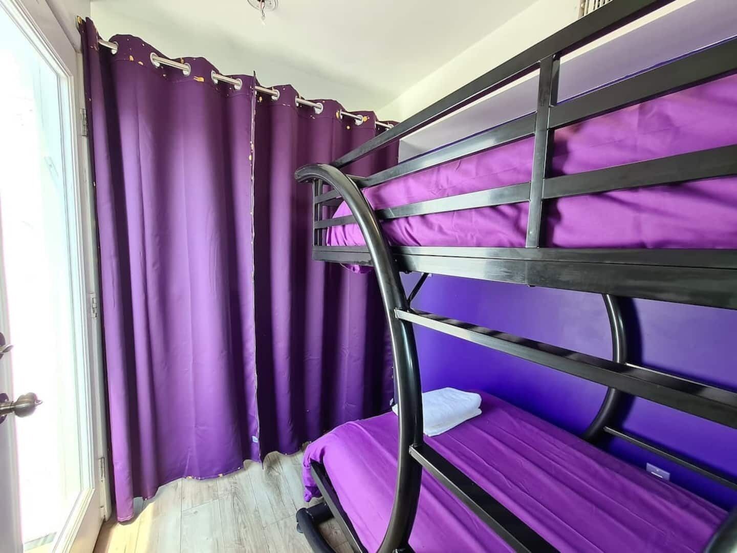 A bunk bed with purple bedding in a room with purple curtains and a wooden floor.