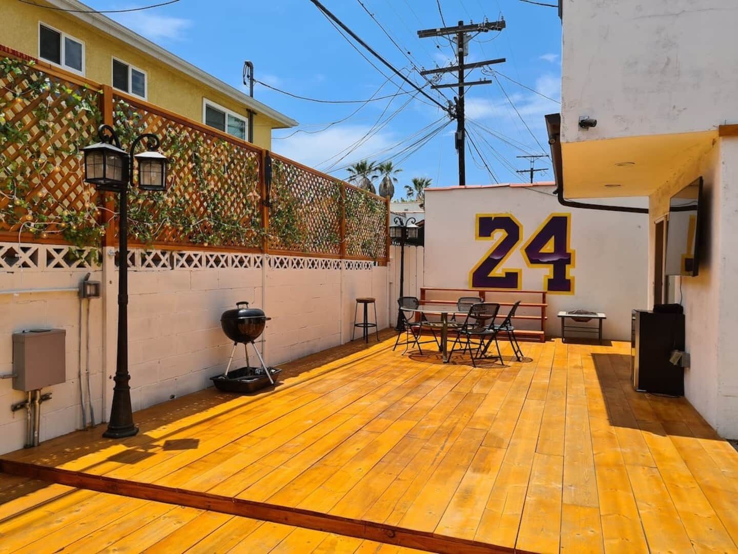 Une terrasse avec une plateforme en bois, un barbecue, des sièges d’extérieur et le chiffre « 24 » peint sur un mur.