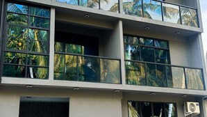 Un immeuble à plusieurs étages doté de grandes fenêtres qui reflètent les palmiers, une enseigne indiquant « SW Residence » et un appareil de climatisation.