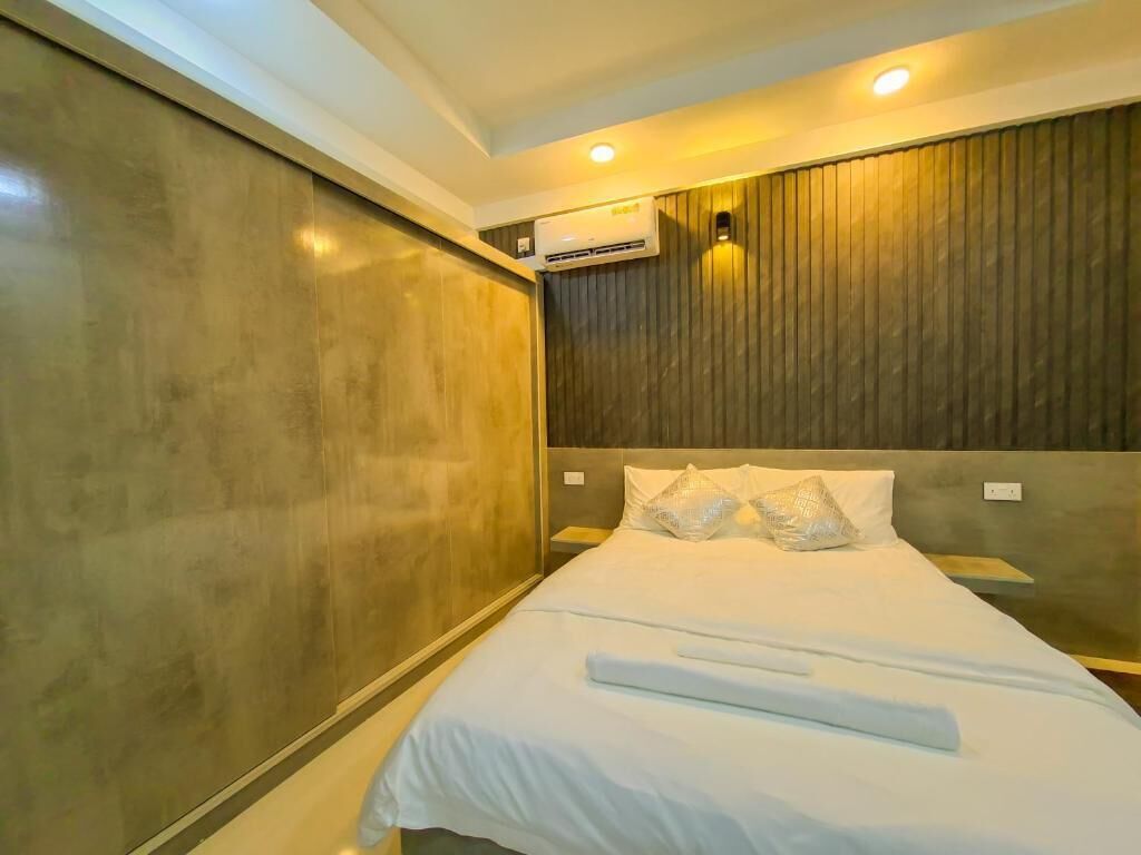 Habitación de hotel con una cama grande, paneles de madera en las paredes, un equipo de aire acondicionado y una mesita de noche.