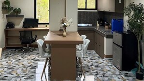 A modern kitchen with a central island, white chairs, a dining table, and a computer setup. - El Nido Loft Apartment (El Nido)