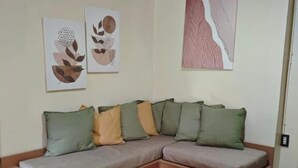 A modern living room with a sectional sofa, a round woven coffee table, and abstract wall art. - El Nido Loft Apartment (El Nido)
