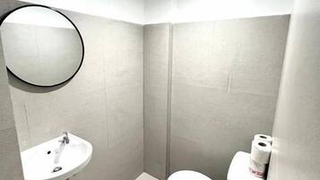 Un baño pequeño y moderno con un espejo redondo, un lavabo y un inodoro.