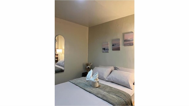 A bedroom with a bed, pillows, a bedside table with a lamp, a mirror, and three framed pictures on the wall. - El Nido Loft Apartment (El Nido)