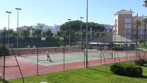 Un court de tennis avec un filet, entouré d’une clôture, et un bâtiment en arrière-plan.