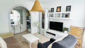 A living room with a TV, sofa, coffee table, and a unique woven light fixture. - Cozy & Spacious apartment near the old town of Tarifa. (Tarifa)