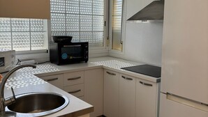 A compact kitchen with white cabinets, a stainless steel sink, a microwave, a black coffee maker, and a white refrigerator. - ISLANTUR BELLAMAR (Lepe)