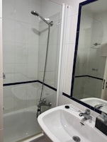 Un baño con ducha, lavamanos y espejo.