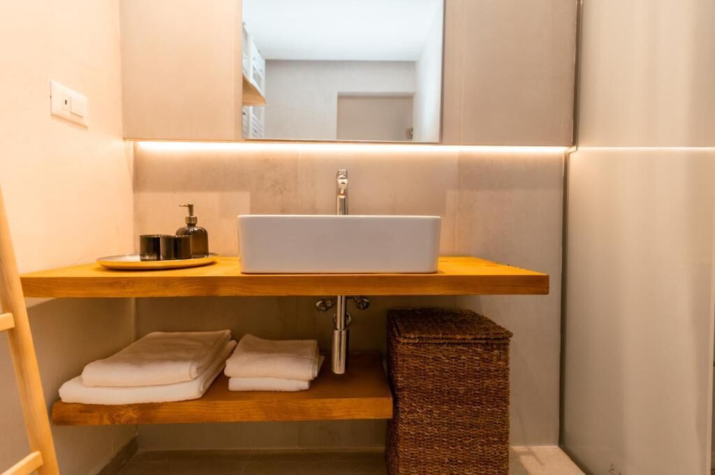 Une salle de bain avec un lavabo blanc, des étagères en bois et un miroir.