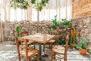 A stone-walled patio with a wooden table and chairs, surrounded by potted plants. - Morpheas Residence (Kos)