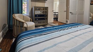 A bedroom with a bed, a chair, a dresser, a TV, and a door.