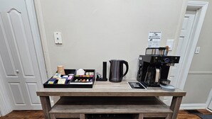 A coffee station with a coffee maker, a kettle, and a tray of coffee pods.