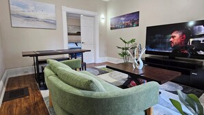 A living room with a green sofa, a dining table, a TV, and artwork on the walls.