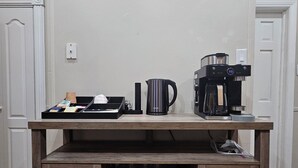 A wooden coffee table with a coffee maker, a kettle, and a tray with cups and a paper bag. Below the table, there are shelves with wine glasses and plates.