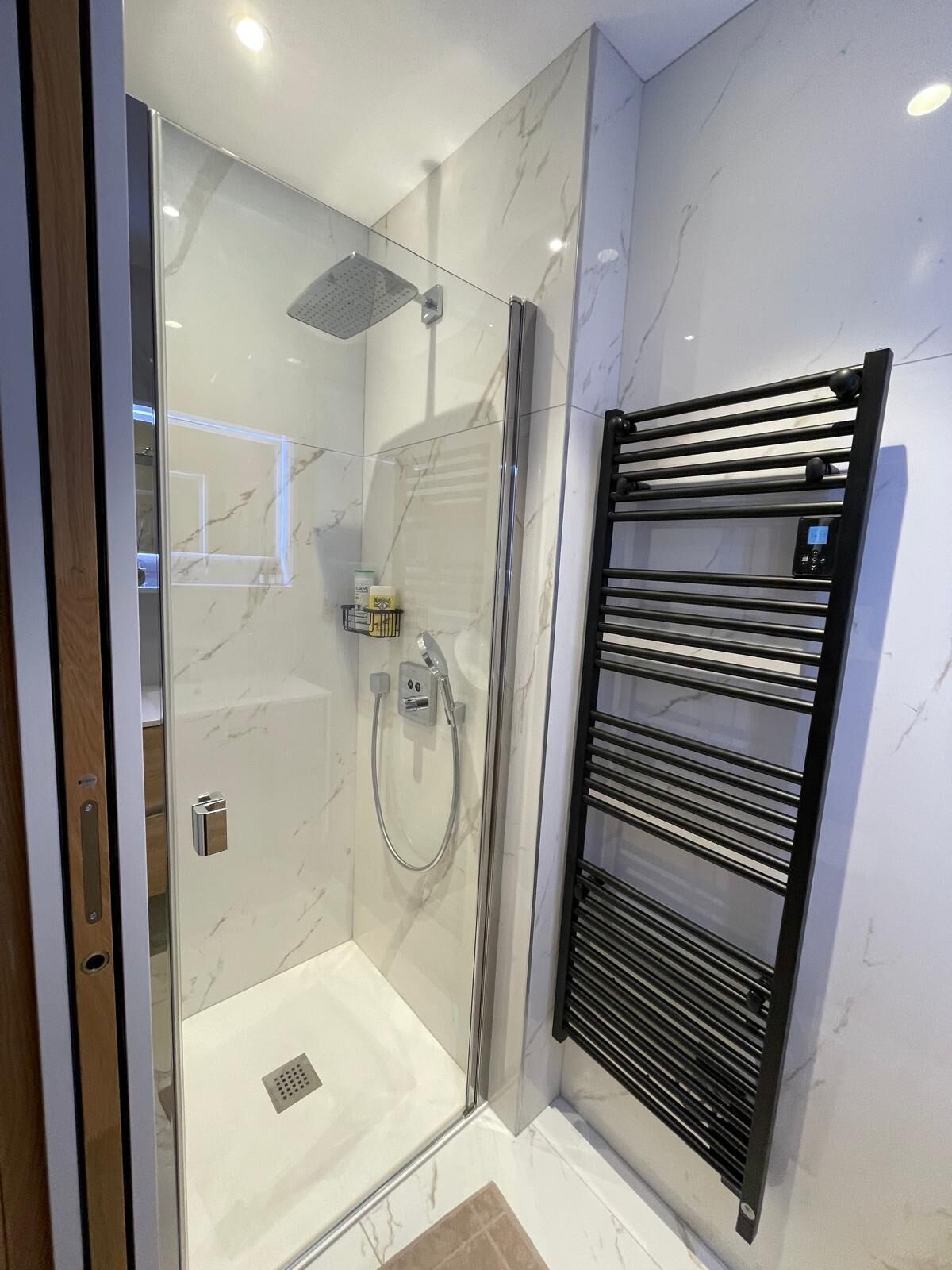 Un baño moderno con ducha de vidrio, toallero negro y pared de mármol.