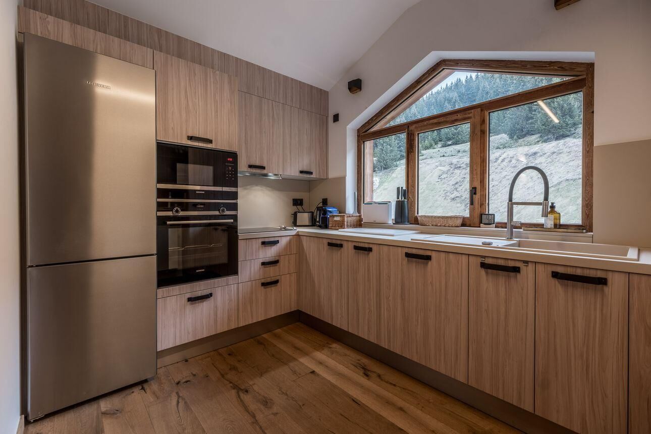 Une cuisine moderne avec des meubles en bois, des appareils électroménagers en acier inoxydable, une grande fenêtre donnant sur un paysage enneigé et un four encastré.