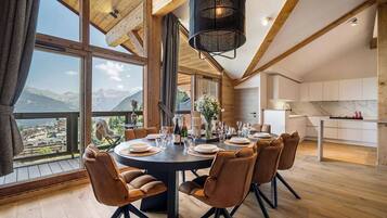 A dining area with a round table, brown chairs, and a view of mountains through large windows.