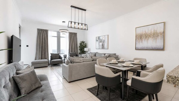 A modern living room with a sofa, armchairs, a dining table with chairs, a TV, and artwork on the walls.