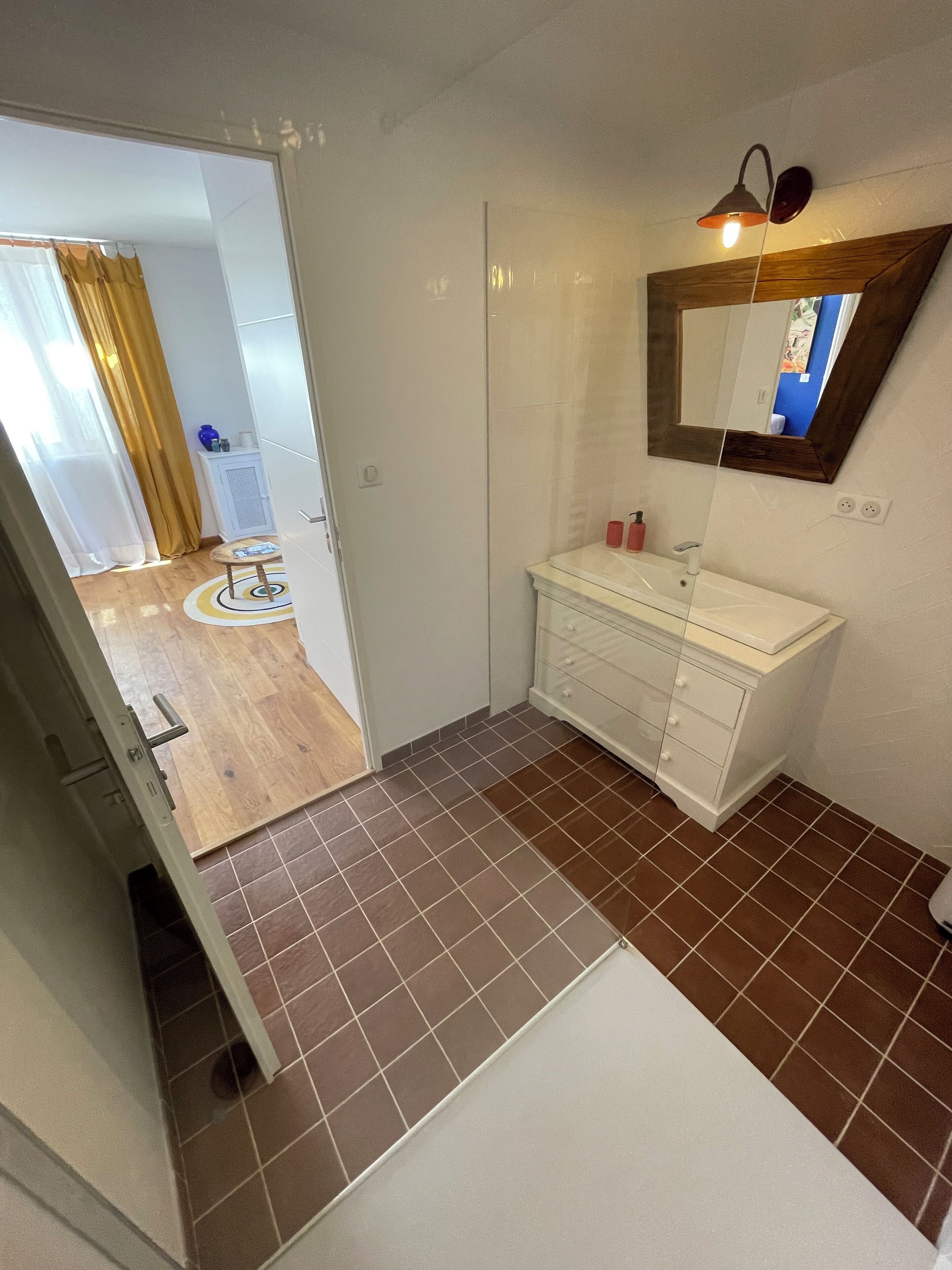 A bathroom with a white vanity, a mirror, and brown tiled flooring.