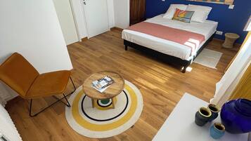 Un dormitorio moderno con una cama, una mesita redonda pequeña, una silla azul y suelo de madera.
