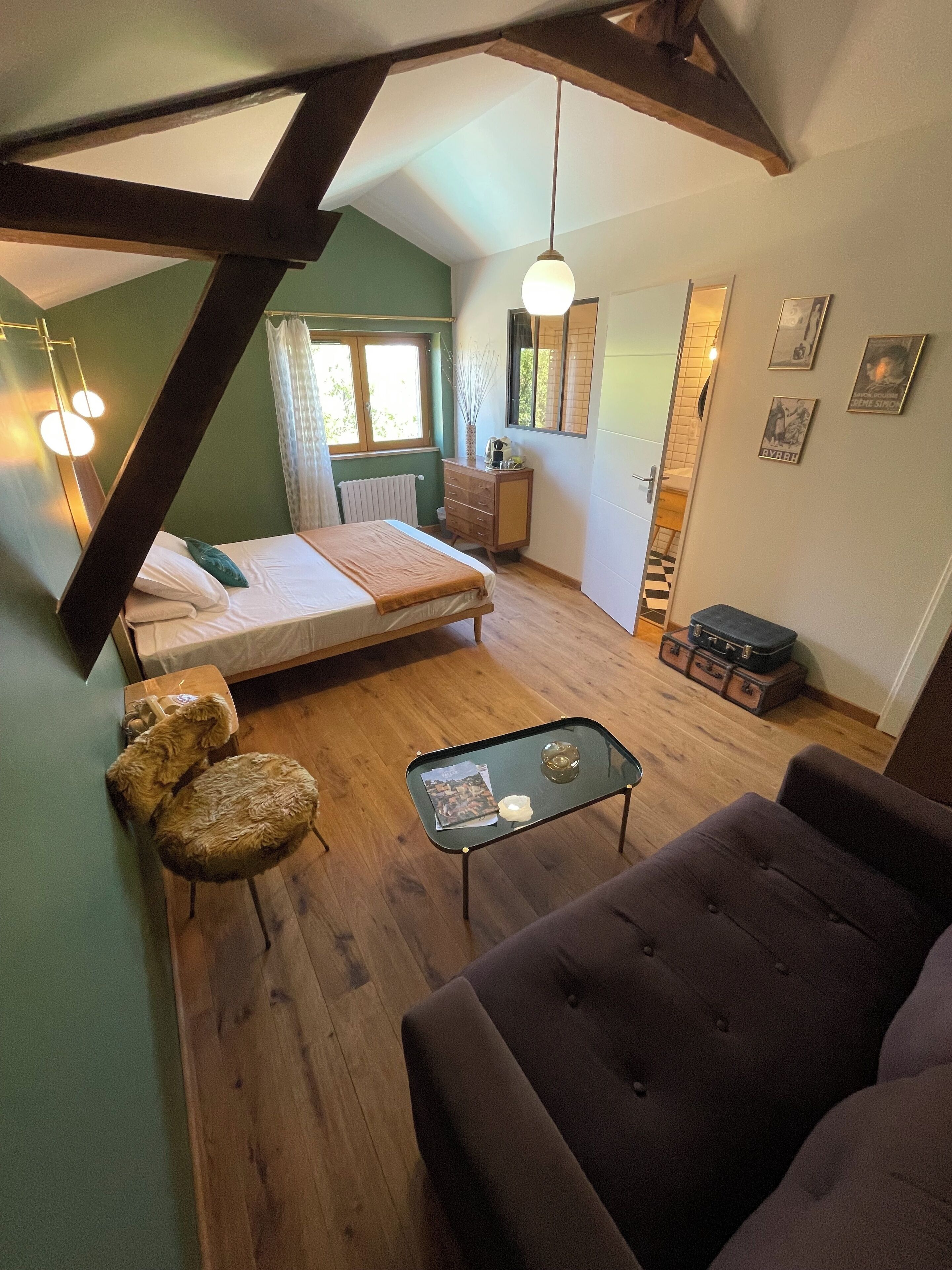 A loft-style bedroom with a bed, a small desk, a sofa, and a dining table.
