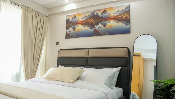 A hotel room with a bed, a large mirror, and a painting of mountains on the wall.