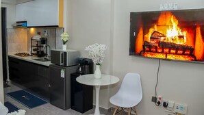 A modern kitchen with a microwave, stove, and coffee maker. There is a white chair and a small table with a vase of flowers. A fireplace with a 'LOVE' sign is on the wall.