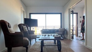 Ein geräumiges Wohnzimmer mit großem Fenster, einem Flachbildfernseher und einem Sofa.