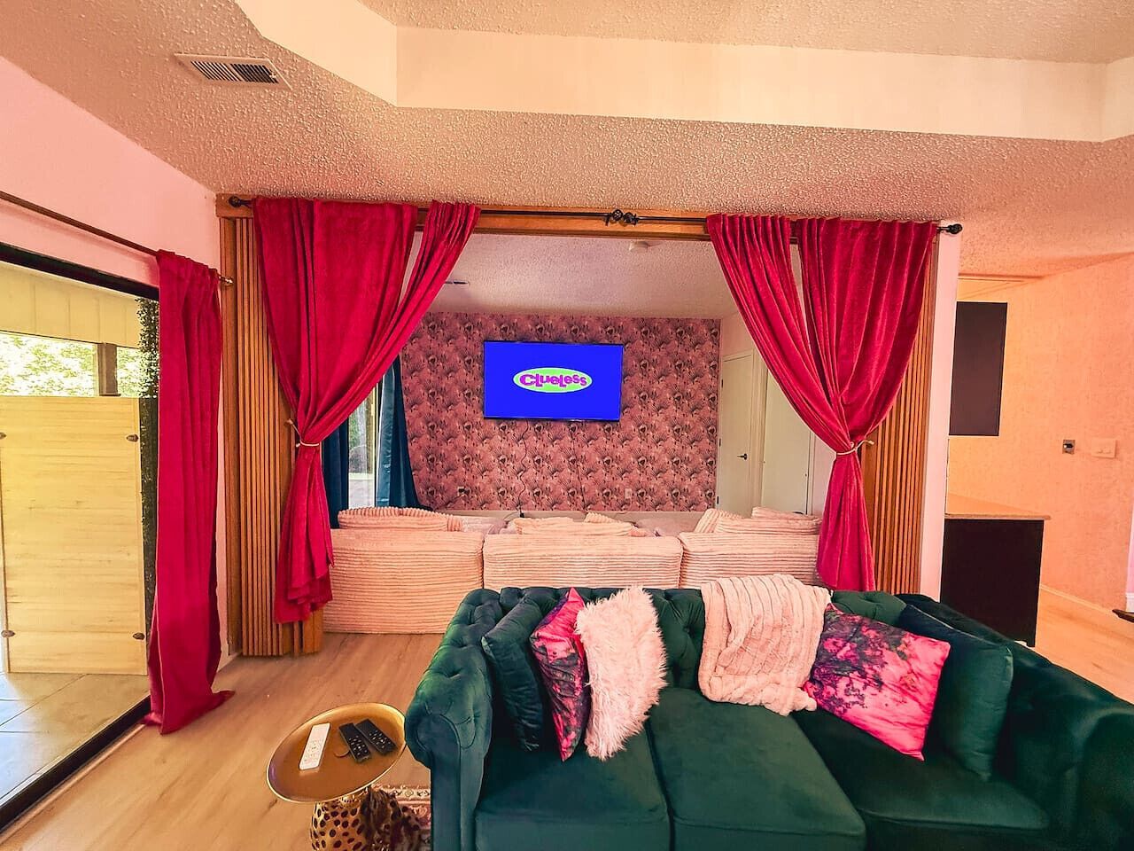 Un salón con un sofá verde, cortinas rojas, un televisor de pantalla plana y una pared con estampado.