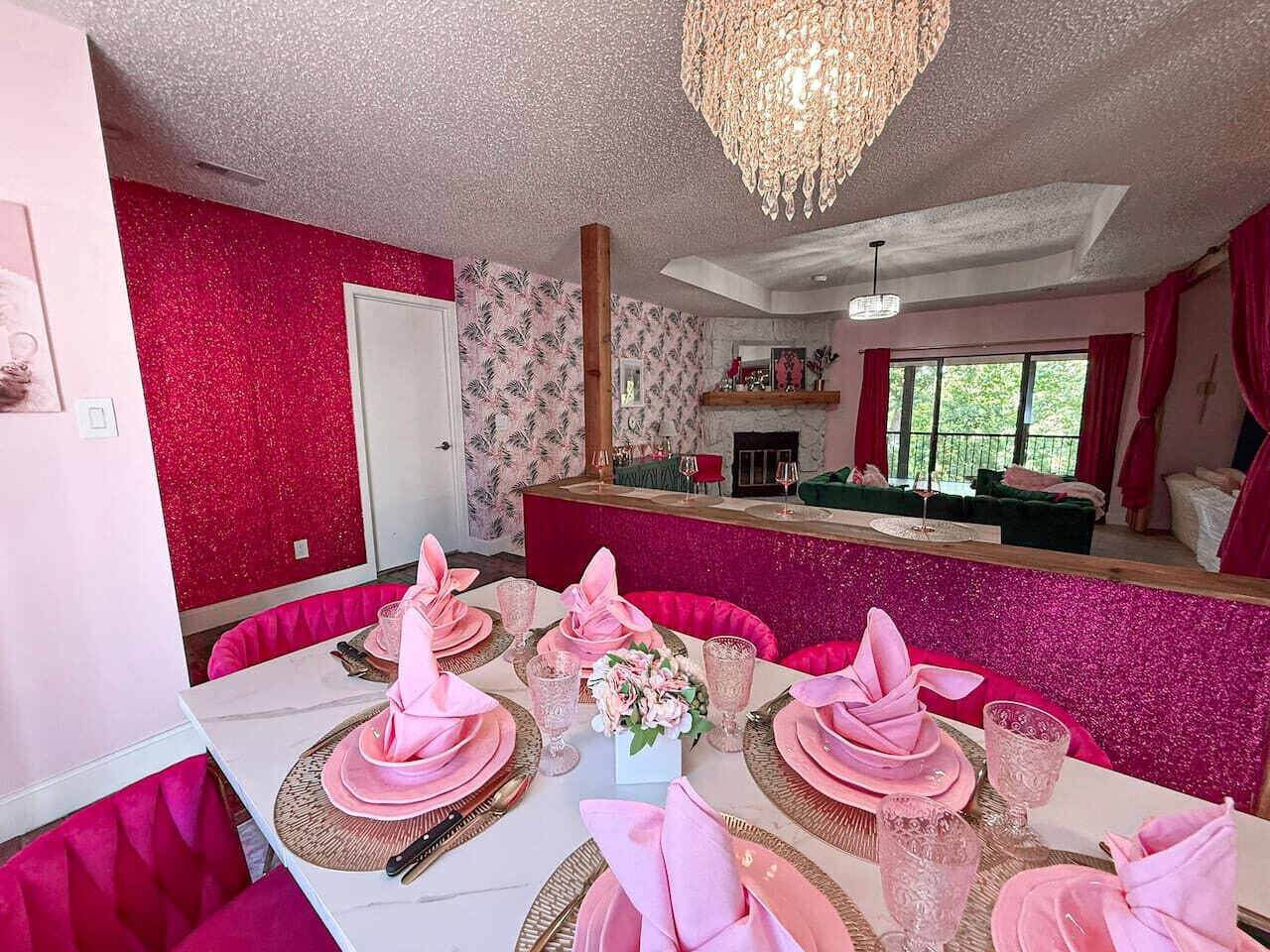 Un comedor con decoración rosa y blanca, una araña y vistas a un sofá verde y una ventana.